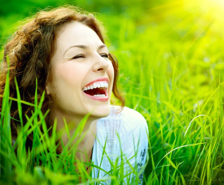 a woman sitting in a grassy field while smiling.